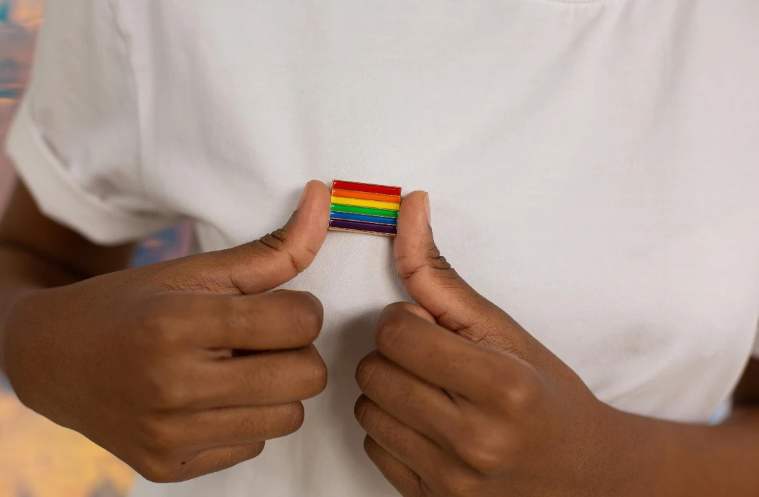 Close-up detail of pride apparel with a rainbow pride pin on a white shirt, showing authentic identity expression instead of generic seasonal branding