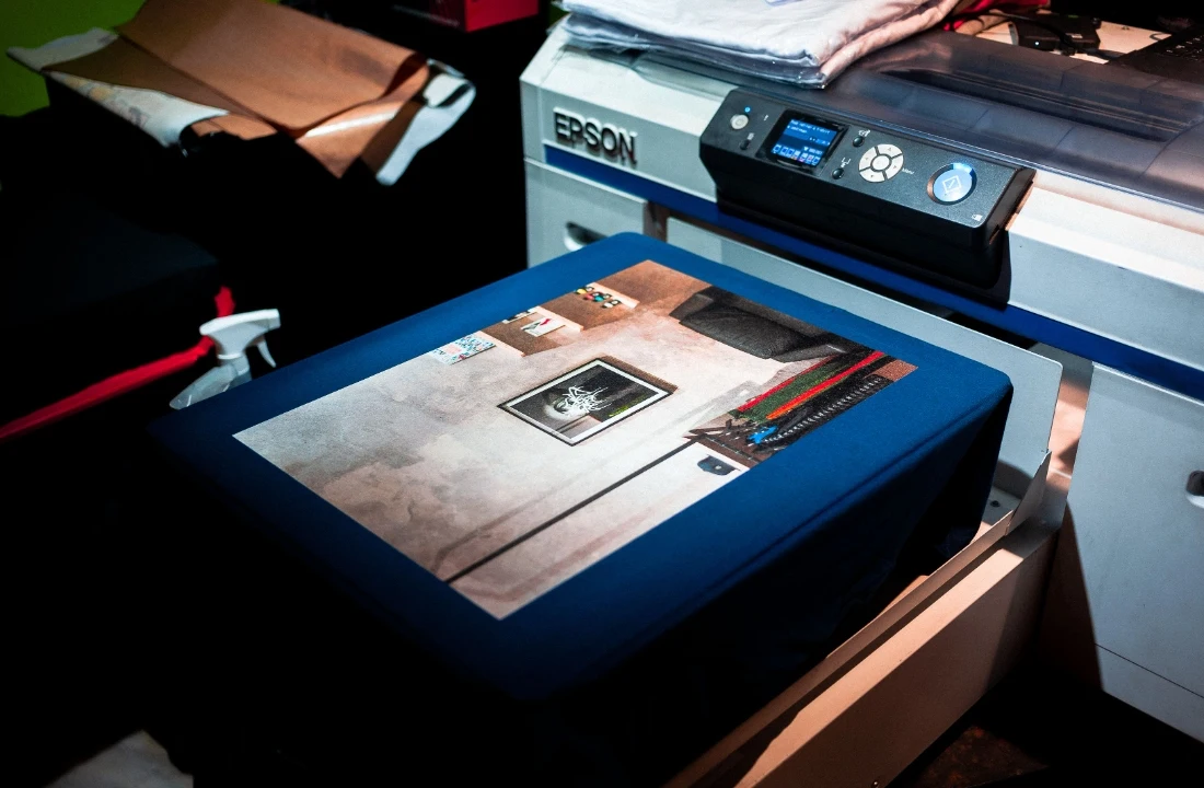 Custom clothing printing image showing artwork being printed on fabric, suitable for discussing fabric choice, ink absorption, print quality, and color performance