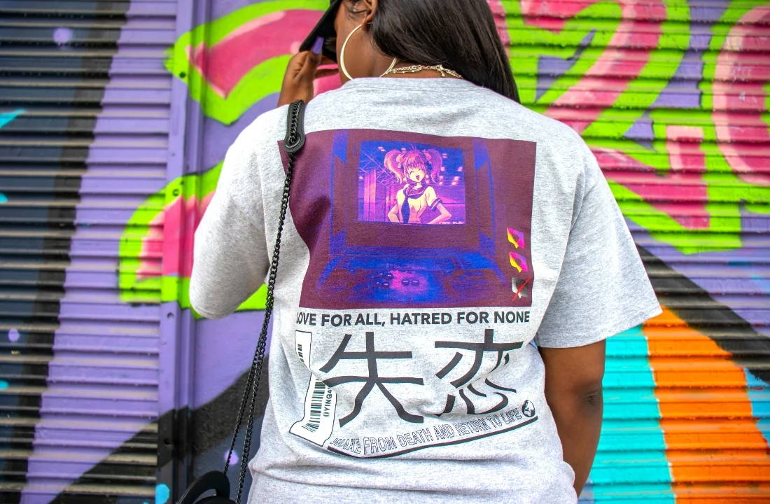 Print on Demand Streetwear image showing a grey back graphic T shirt worn in front of colorful graffiti, suitable for streetwear brand design inspiration