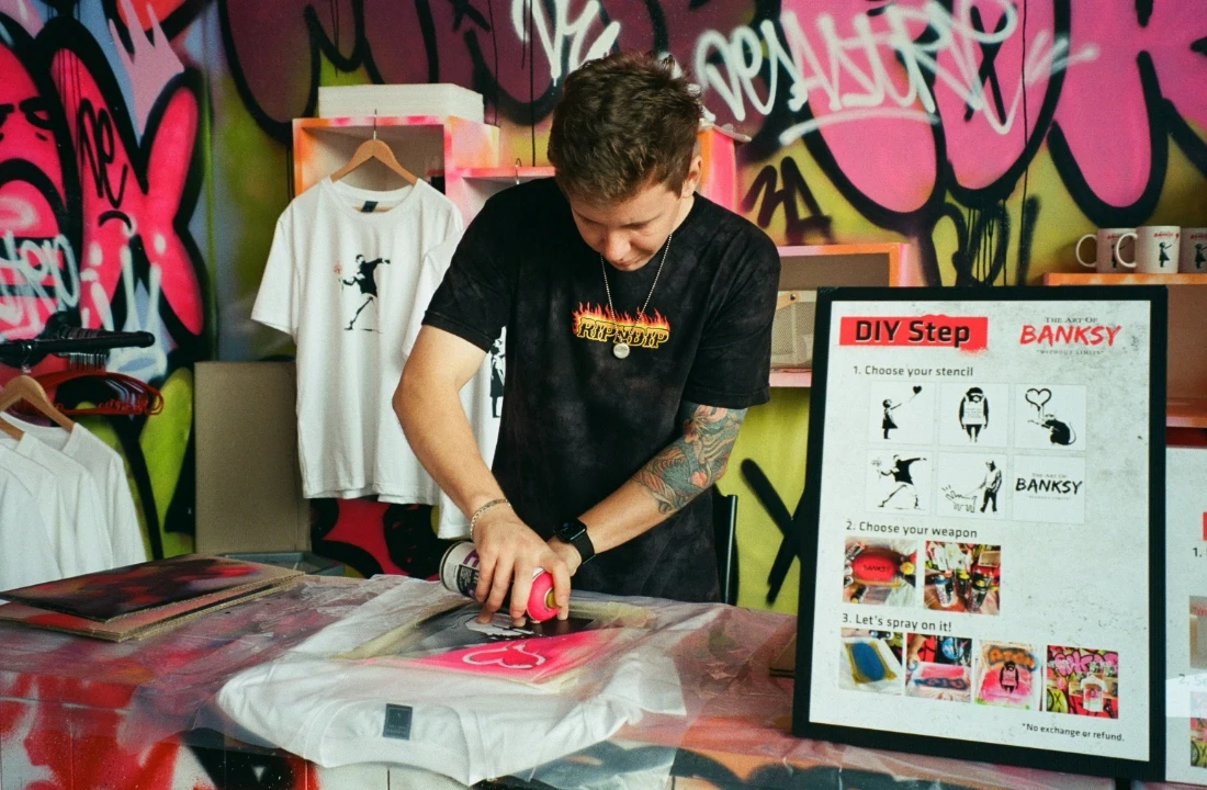 Print on Demand Streetwear production image showing a custom T shirt being spray printed in a workshop, suitable for POD apparel printing and design process content
