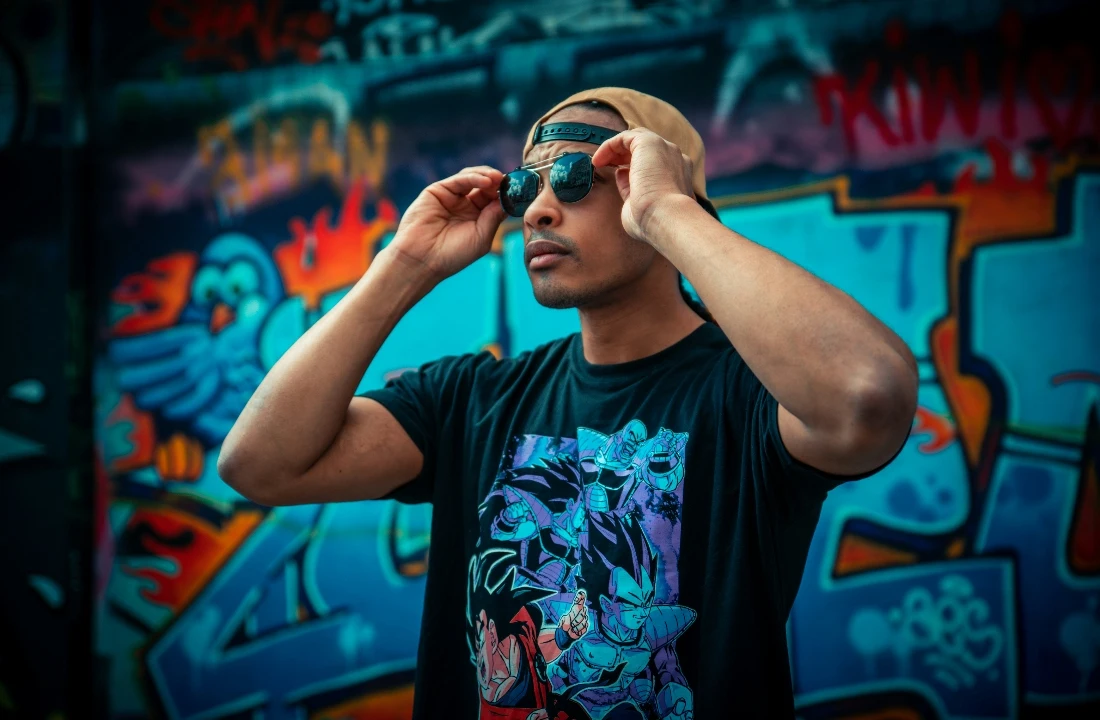 Print on Demand Streetwear image showing a black graphic T shirt in front of a graffiti wall, suitable for bold streetwear prints, custom tee design, and urban apparel branding
