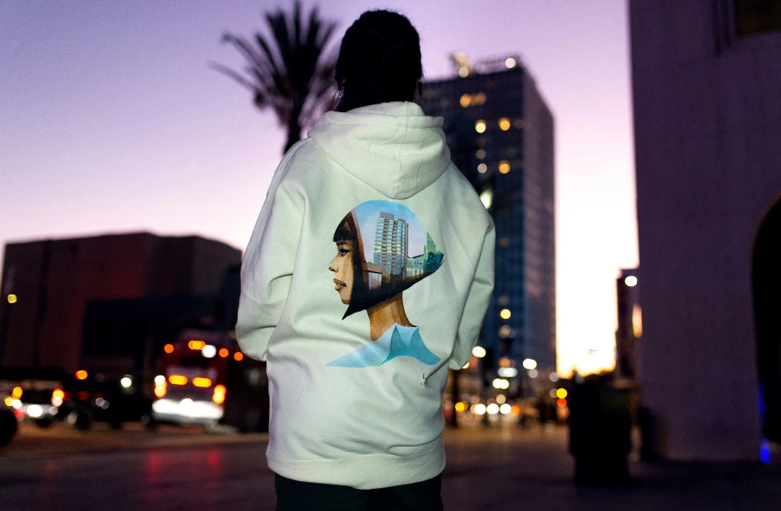 Print on Demand Streetwear image showing a white hoodie with a large back graphic in an urban evening setting, suitable for custom hoodie design and streetwear brand collections