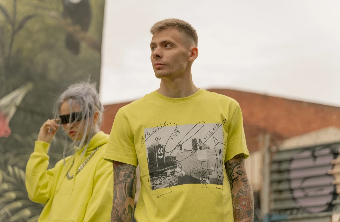 Tattooed model wearing a yellow Print on Demand Streetwear graphic T-shirt with a matching hoodie styled in the background