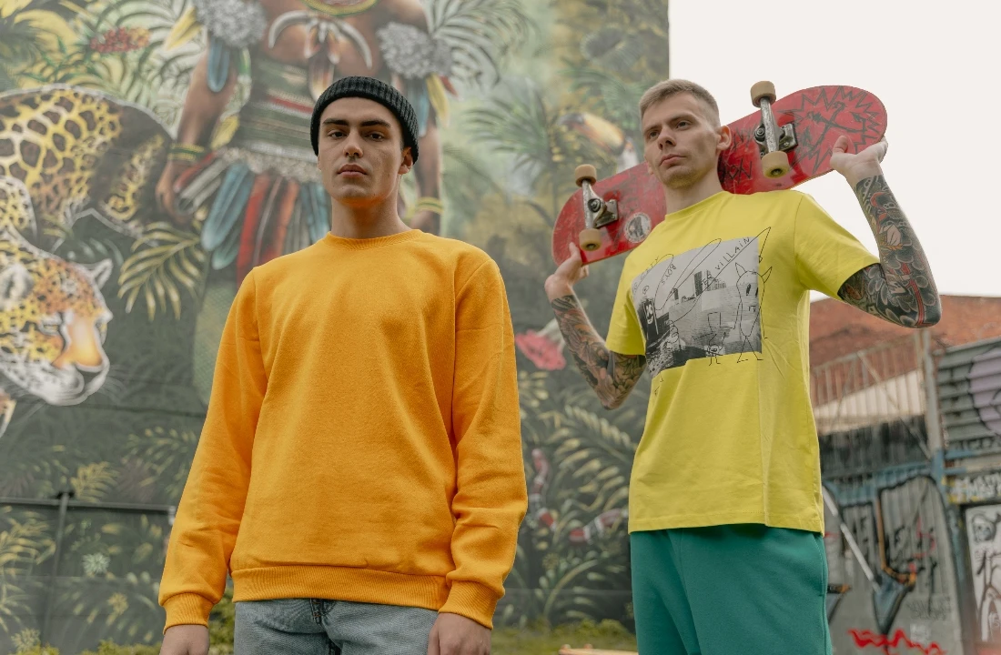 Two skateboarders wearing bright yellow and orange apparel in an urban setting, representing a youth-focused POD Streetwear collection