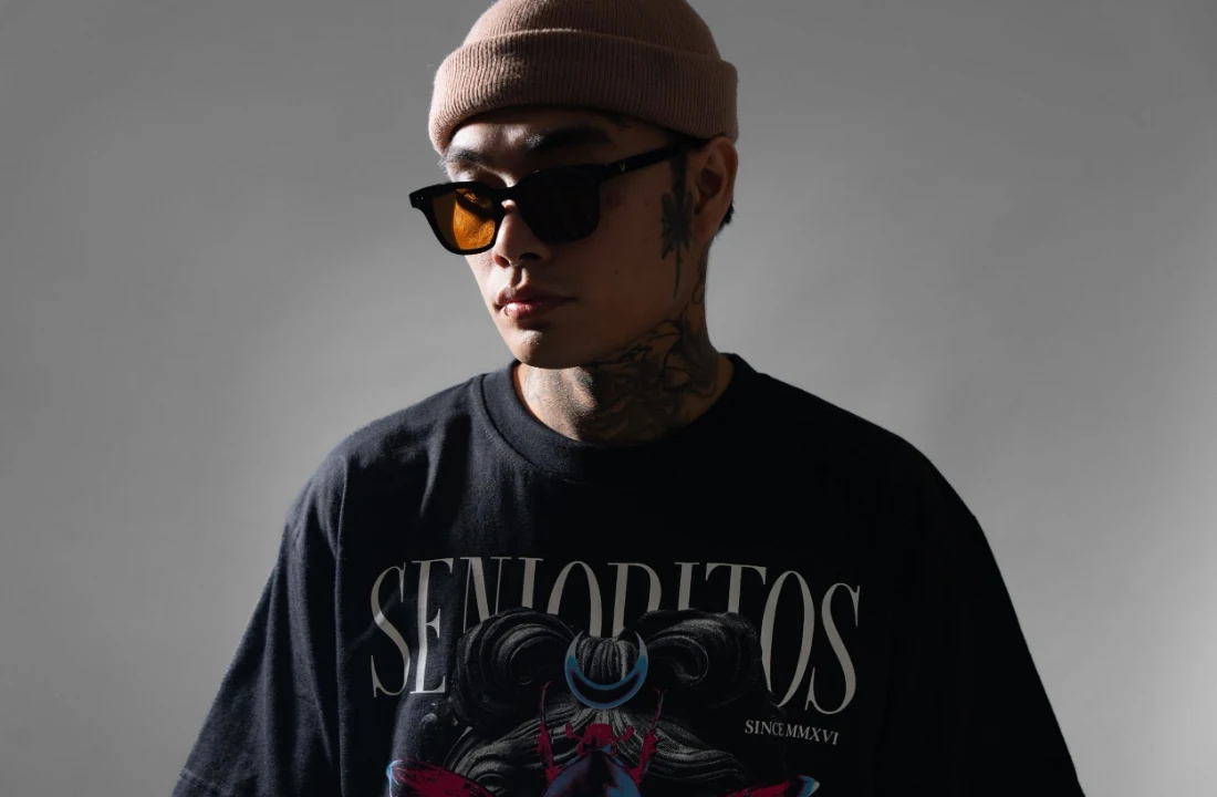 Man wearing a black graphic oversized T-shirt with a beanie and sunglasses in a studio setting