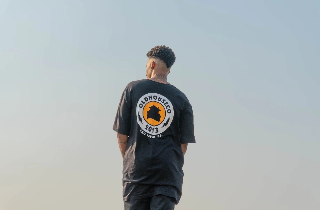 Man wearing a black oversized T-shirt with a large circular back print against an open sky
