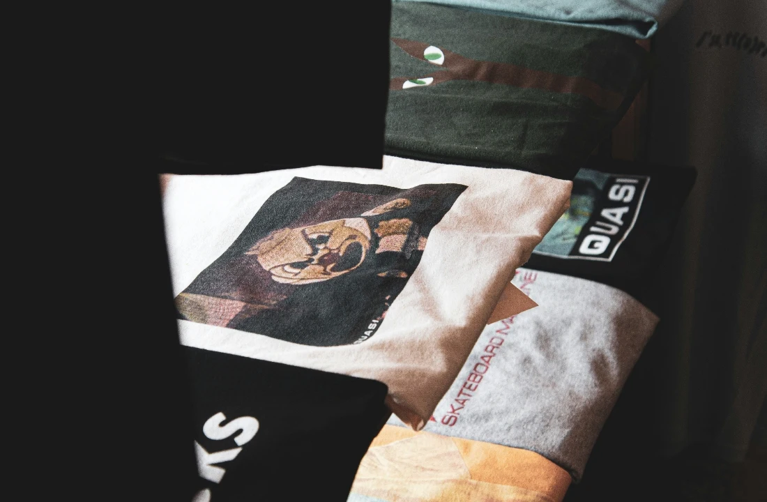 Stack of folded graphic boxy tees featuring assorted prints and neutral fabric colors