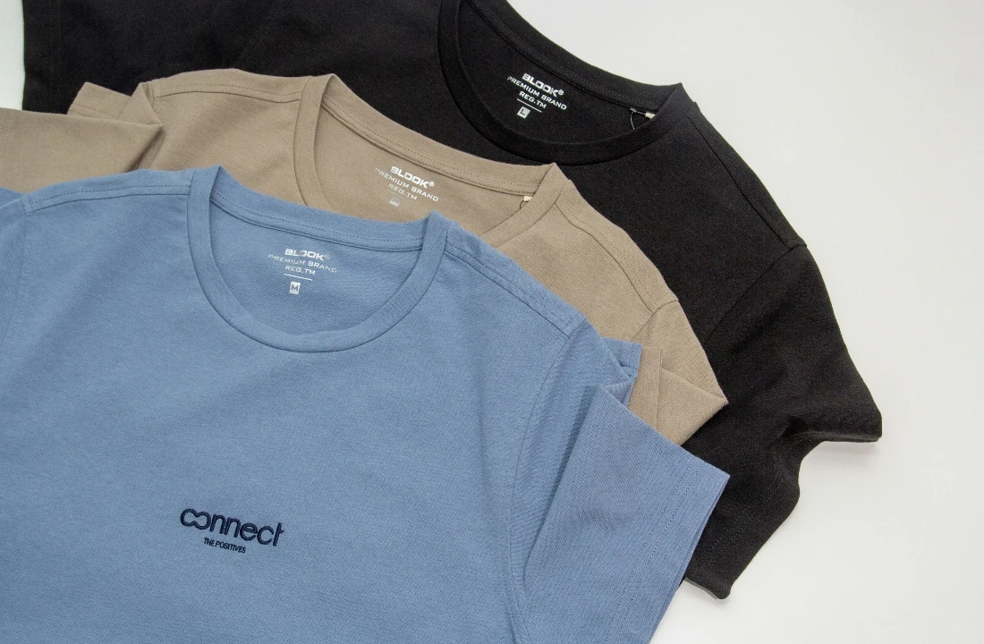 Blue, beige and black boxy tees arranged flat to show their relaxed shape and crew neck construction