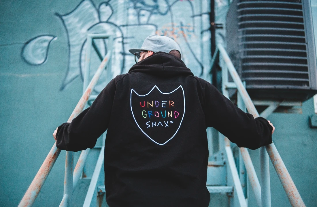 Back view of a person wearing a black hoodie with a minimalist outlined logo on an industrial staircase