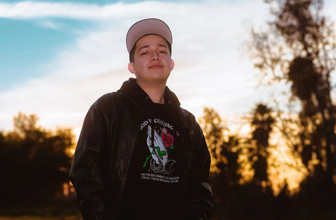 Person wearing a black graphic hoodie beneath a leather jacket outdoors during sunset