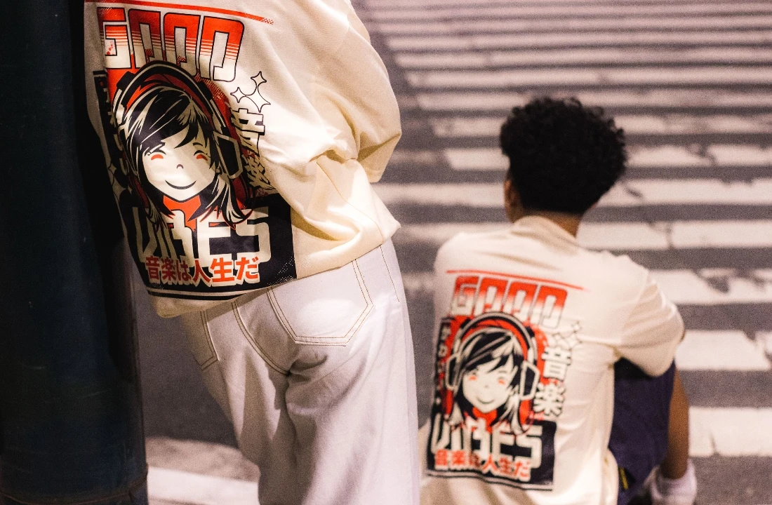 Two people wearing matching cream graphic T-shirts with oversized back prints in an urban street setting