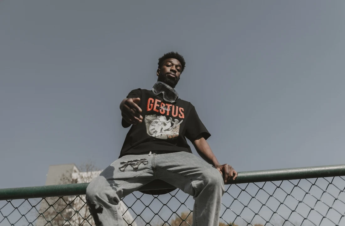 Man sitting on a fence wearing an oversized black print on demand streetwear T-shirt with a bold graphic print