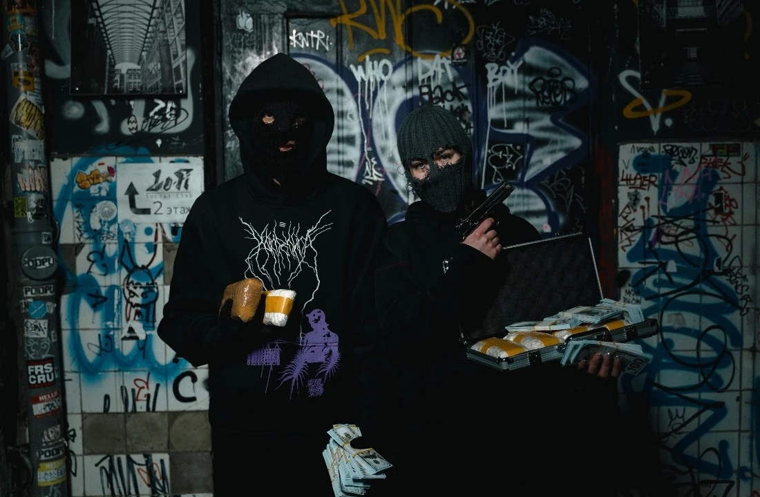 Two people in black POD Streetwear hoodies standing in a graffiti-covered urban setting, with bold graphic prints on the garments