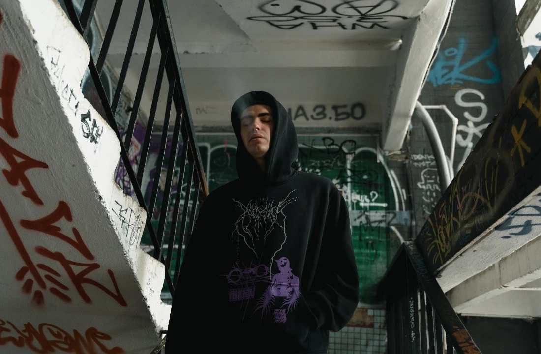Person wearing a black POD Streetwear hoodie with a front graphic design, standing in a graffiti-covered stairwell