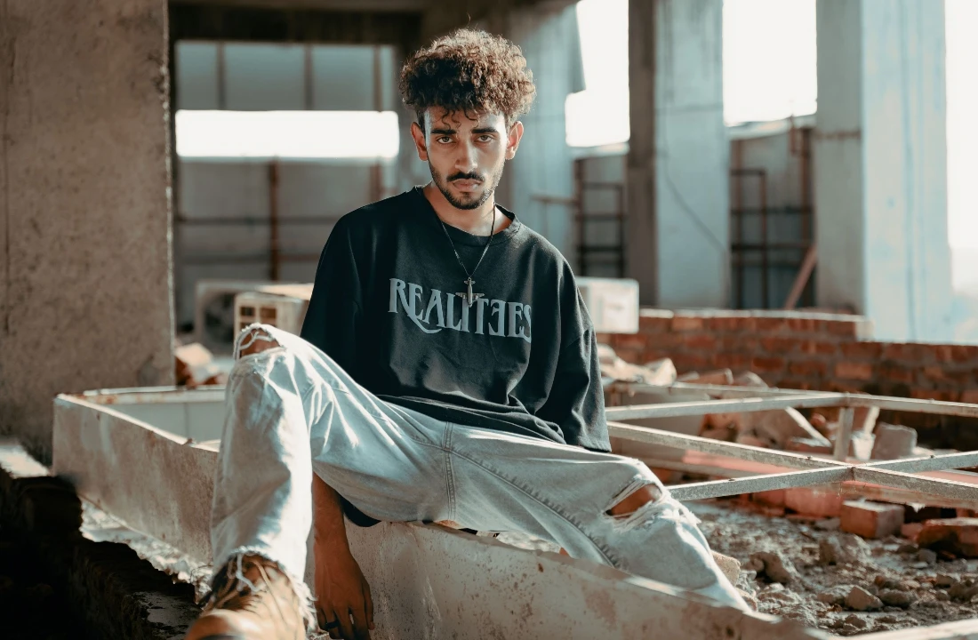 Person sitting in an industrial space wearing an oversized black POD Streetwear T-shirt with minimalist front lettering