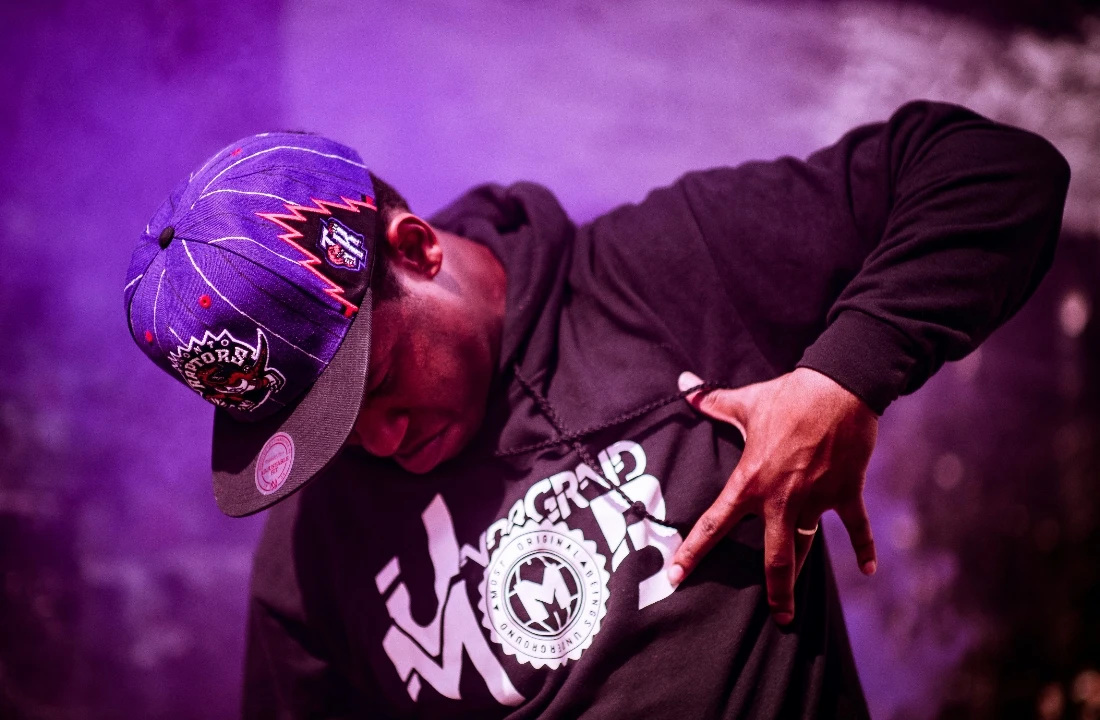 Person wearing a black Streetwear Print on Demand hoodie and cap in a purple-lit urban scene
