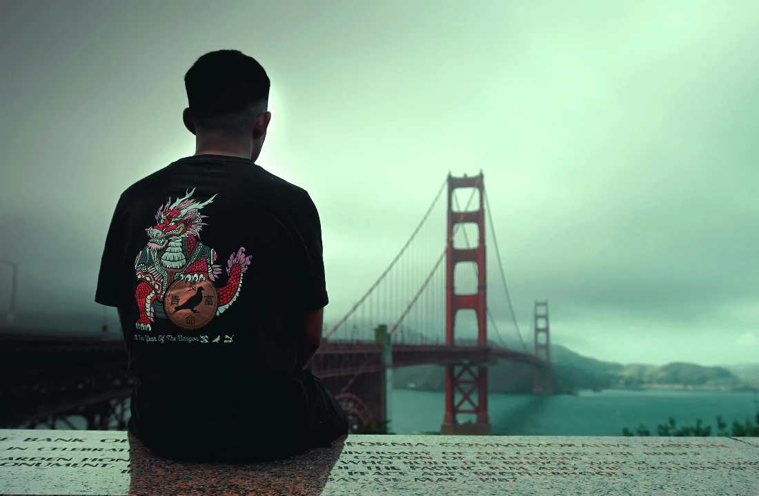 Back view of a person wearing a black Streetwear Print on Demand T-shirt with a dragon graphic near the Golden Gate Bridge