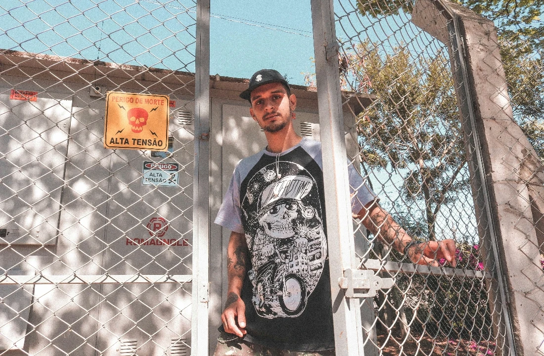 Man standing by a chain-link fence wearing a Streetwear Print on Demand skull graphic raglan T-shirt
