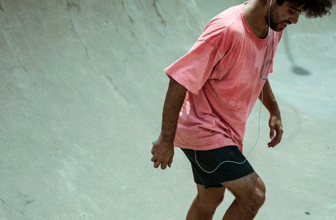 A man wearing a relaxed pink Heavyweight Cotton T Shirt with black shorts in a concrete skatepark