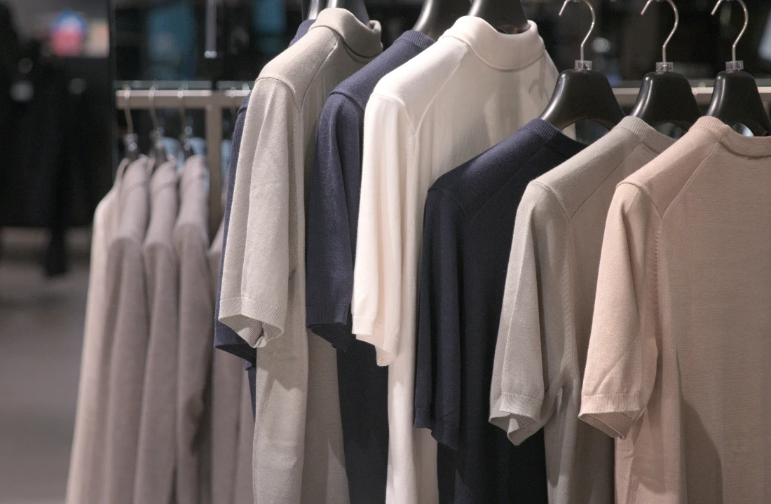 A store rack displaying neutral Heavyweight Cotton T Shirts in black, white, beige, and navy tones