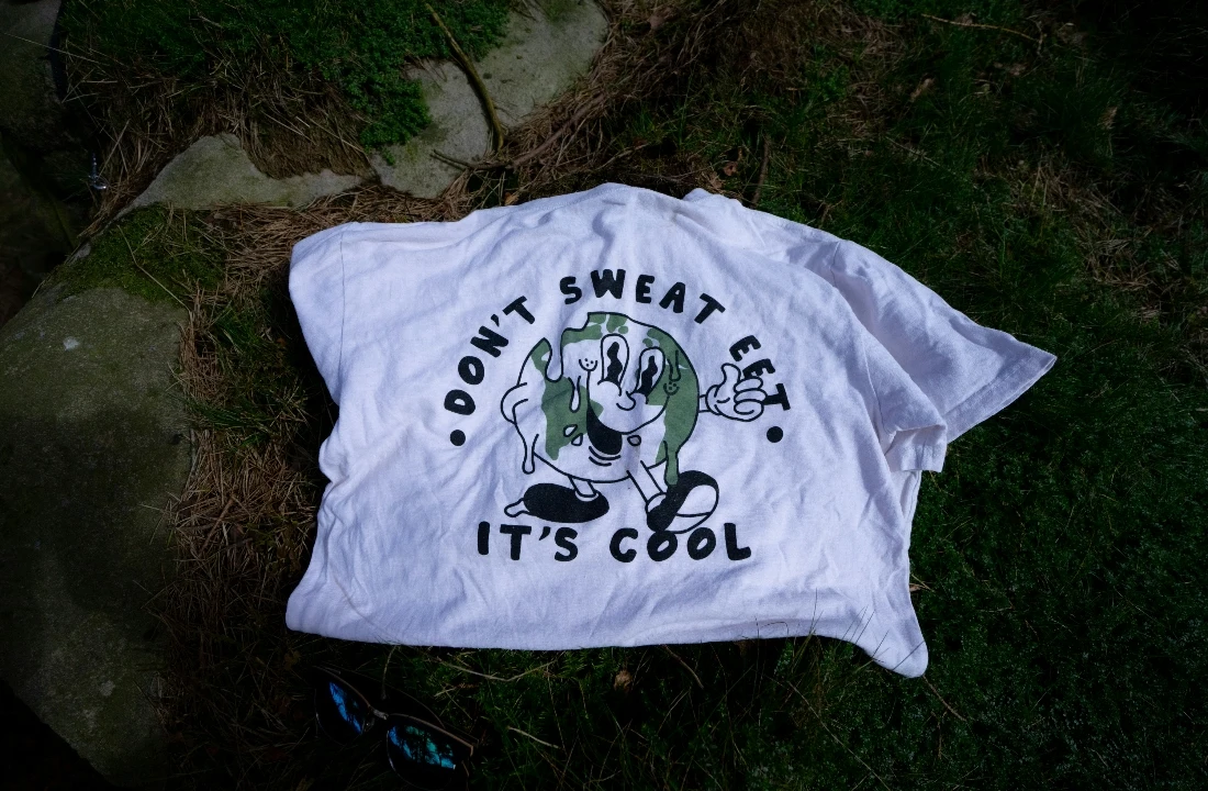 A white Heavyweight Cotton T Shirt with a casual graphic print laid flat on grass and stones