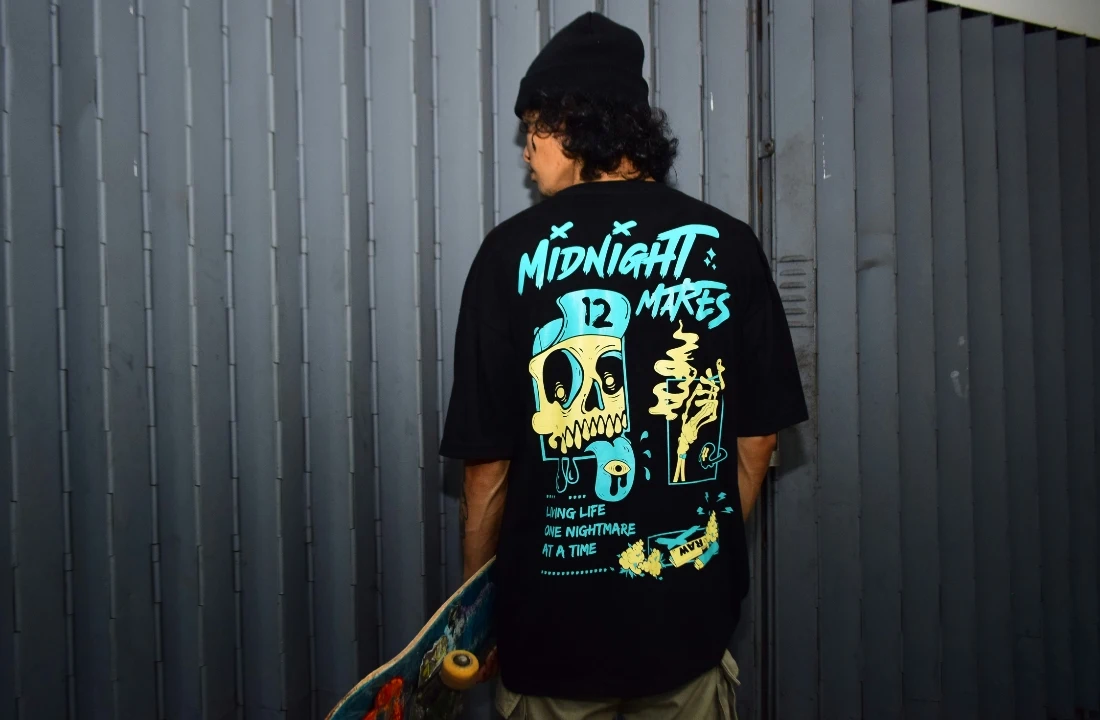 A person wearing an oversized black Print on Demand Streetwear T-shirt with a large skull back print and holding a skateboard