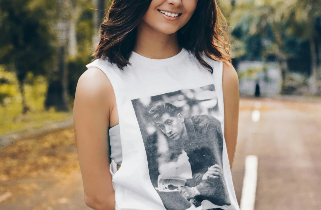 A smiling woman wearing a white sleeveless Print on Demand Streetwear tee with a black-and-white portrait graphic outdoors