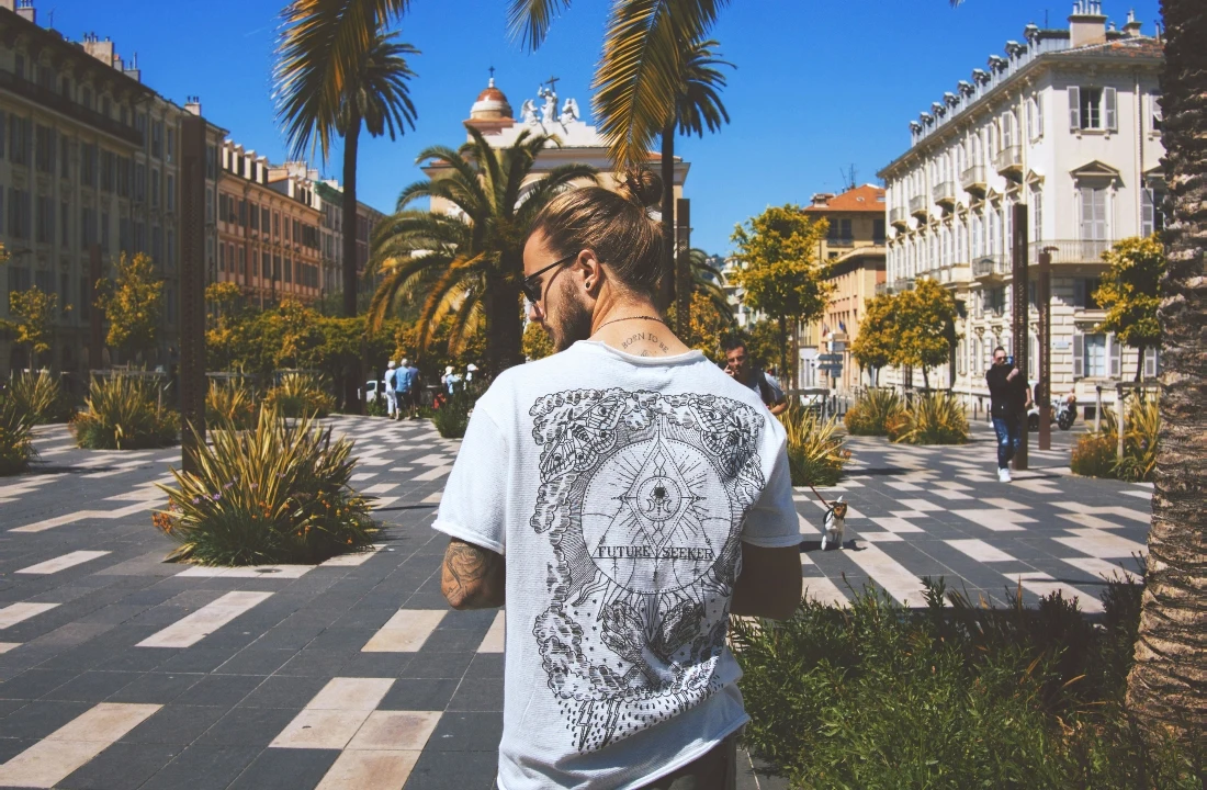 A man walking outdoors in a white Print on Demand Streetwear T-shirt featuring a detailed back graphic design