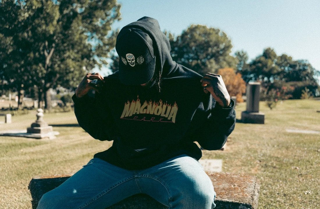 A person sitting outdoors wearing a black Custom Streetwear Hoodies design with a bold front graphic and casual streetwear styling