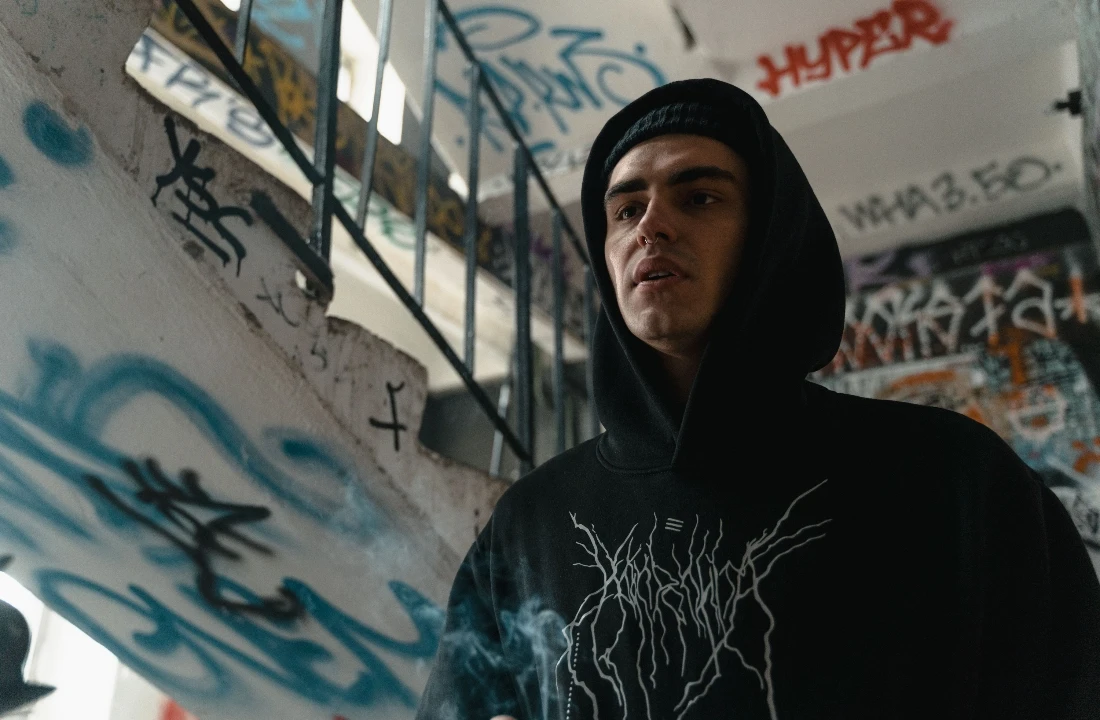 A person in a graffiti-covered stairwell wearing a black Custom Streetwear Hoodies piece with an edgy front graphic