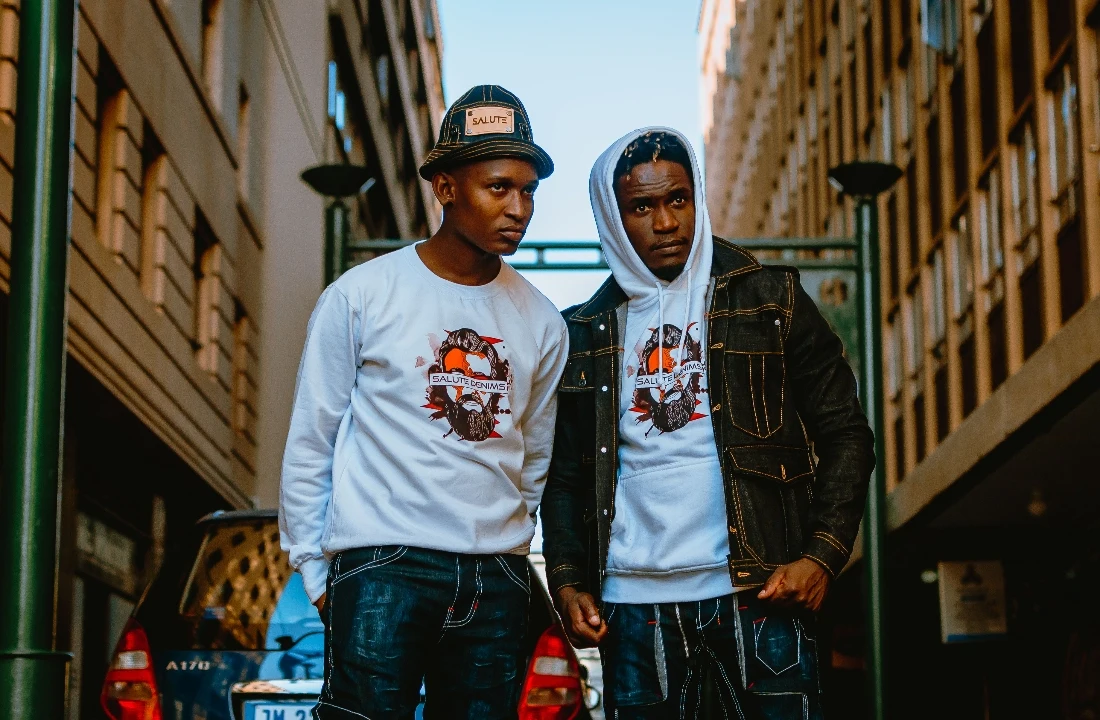 Two men in a city street outfit featuring Custom Streetwear Hoodies styling, including a white graphic hoodie layered under a denim jacket