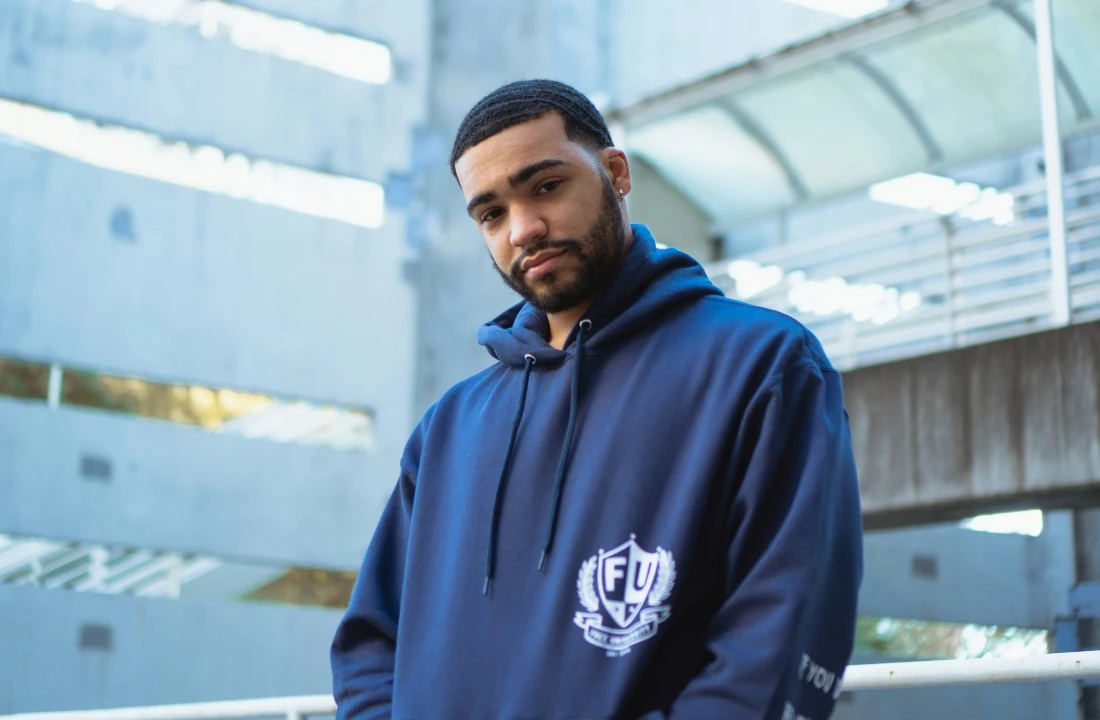 Front view of a man wearing a navy Custom Streetwear Hoodies pullover with a small chest logo in an urban setting