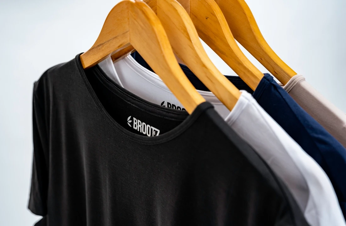 Close-up of Organic Cotton Custom T Shirts in black, white, navy, and beige hanging on wooden hangers