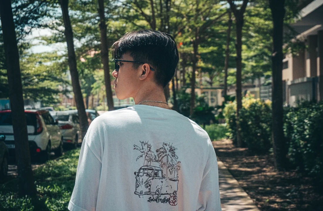 Side-back view of a model wearing boxy fit t shirts with a small back illustration on a shaded street