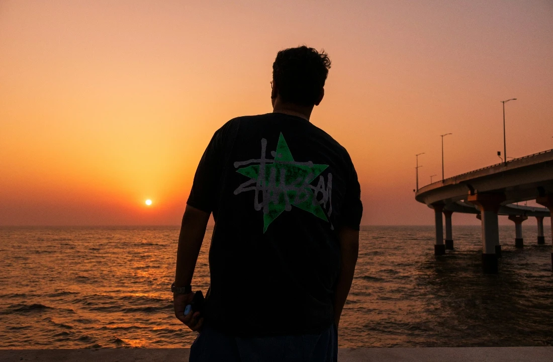Back view of a model wearing boxy fit t shirts with a large graphic print near the ocean at sunset