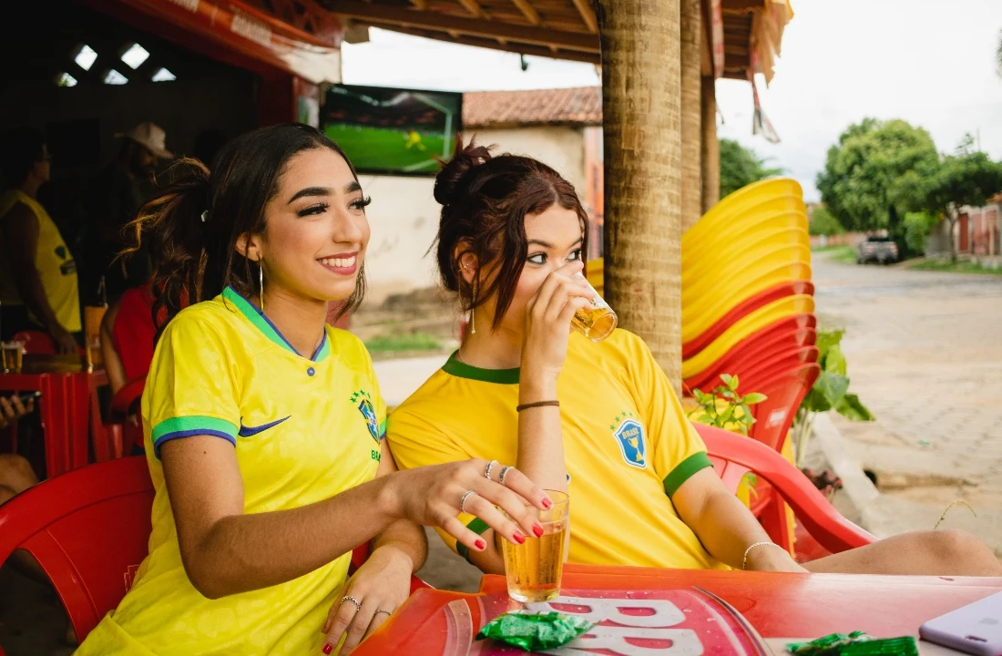 Two women wearing yellow custom football shirts while watching a football match at an outdoor local venue