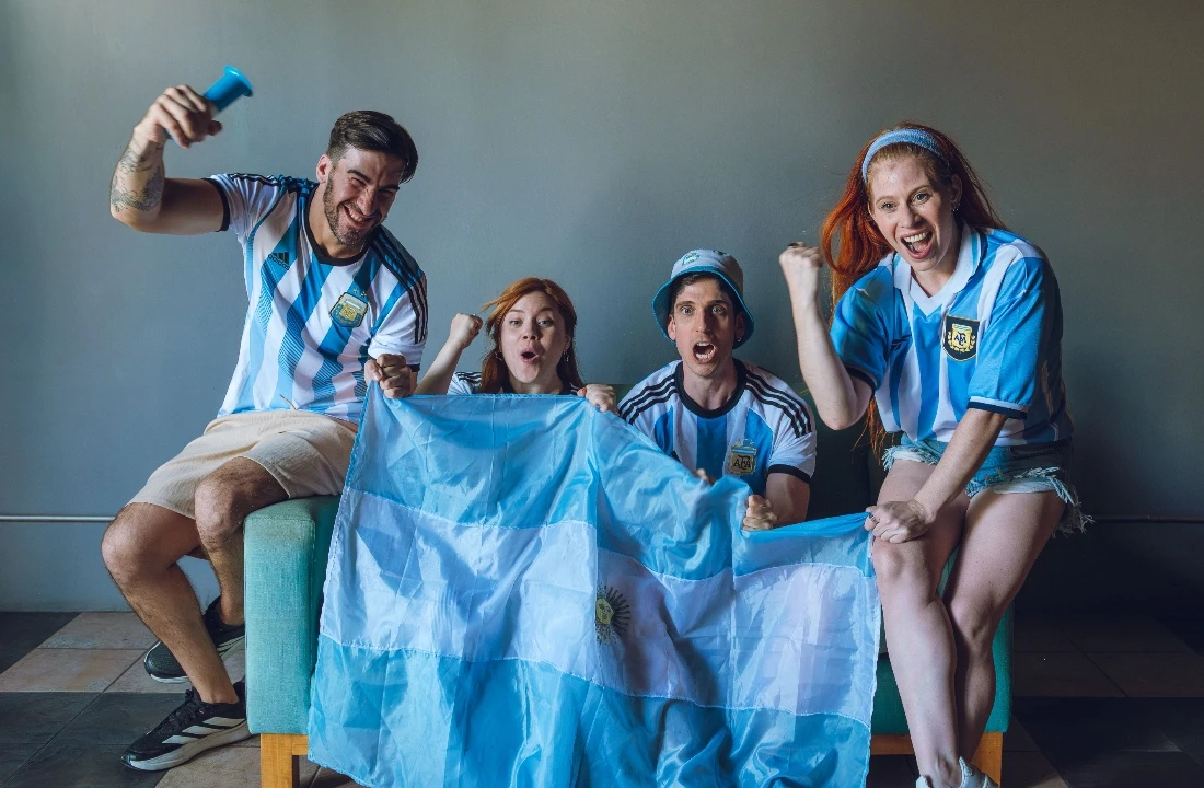 Group of fans wearing blue and white custom football shirts while celebrating a football match indoors