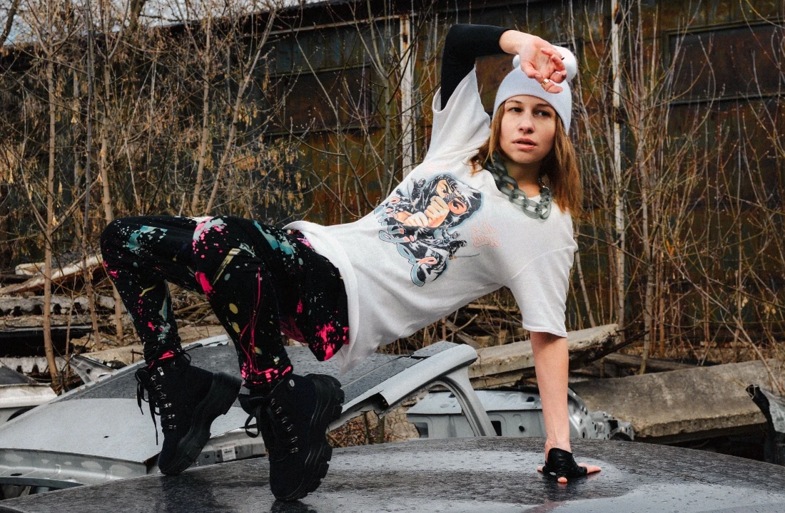 Woman posing in a white graphic tee with printed pants in an abandoned outdoor scene for Grunge Streetwear styling