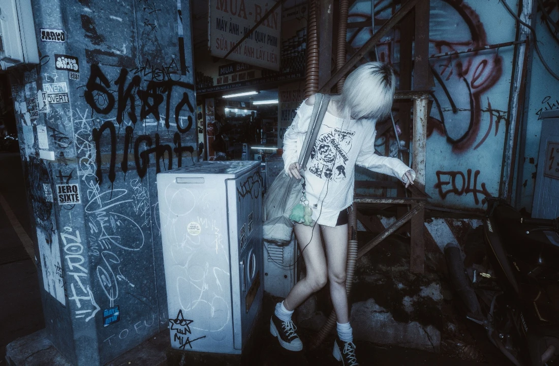 Person wearing a white graphic long sleeve shirt in a graffiti-covered alley for Grunge Streetwear inspiration
