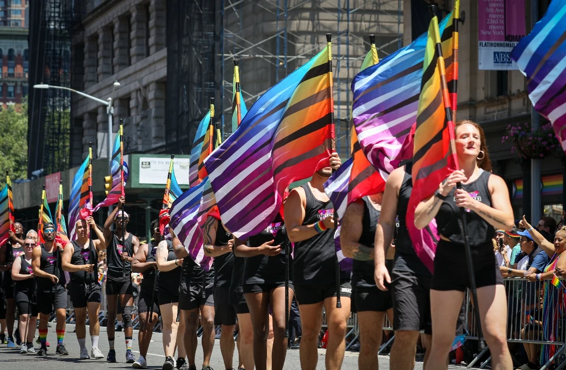 Pride parade participants carrying rainbow flags and wearing coordinated Pride Apparel in a city street event