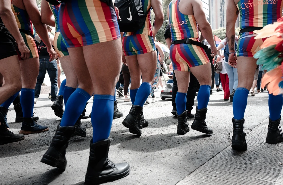 Parade participants wearing rainbow striped Pride Apparel and blue boots during a public celebration