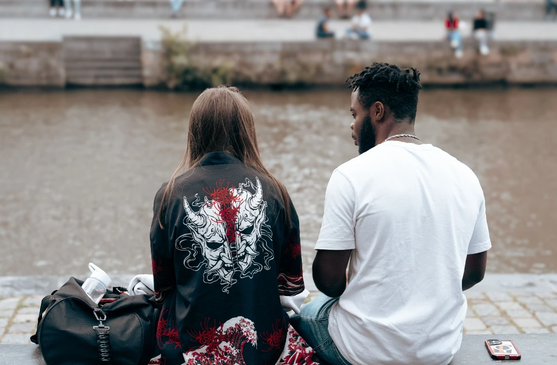 Two people sitting by the riverside in casual print on demand streetwear, featuring a graphic outer layer and a plain white tee