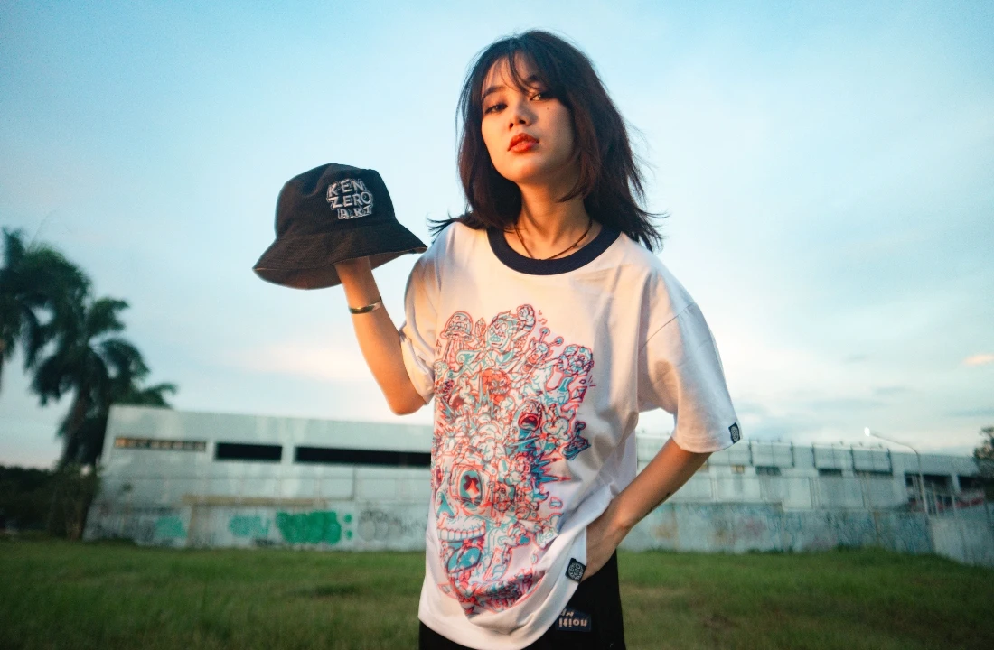 Woman modeling a white print on demand streetwear ringer T shirt with an oversized graphic print and bucket hat outdoors