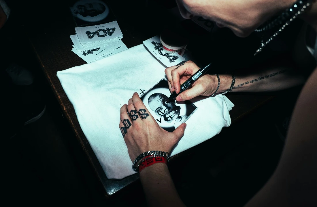 Hands signing a custom label on folded Custom Graphic Tees for limited drop or creator merchandise presentation