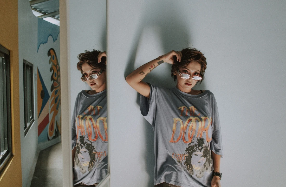 Person wearing Custom Graphic Tees with a vintage-style front print, reflected in a hallway mirror for streetwear styling