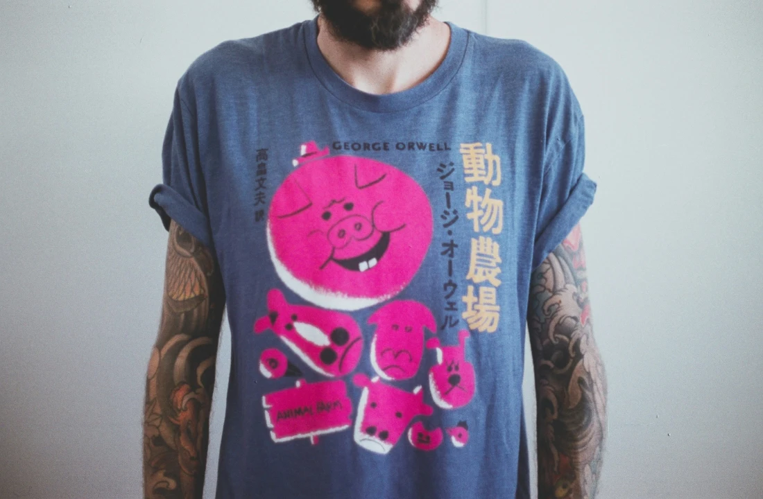 Close-up of Custom Graphic Tees with bold cartoon artwork on a blue shirt, worn by a tattooed person