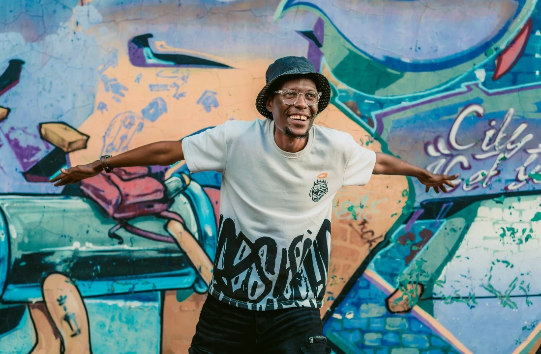 Man wearing a graphic streetwear T-shirt in front of a graffiti wall, showing apparel style supported by a print on demand supplier