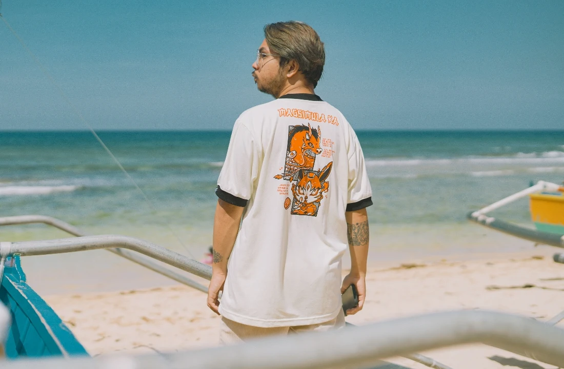 Man wearing a back-print graphic T-shirt near the beach, suitable for lifestyle promotion from a print on demand supplier