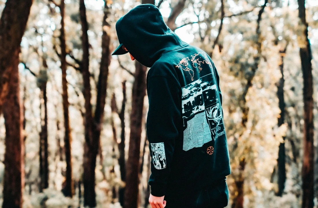 Person wearing a printed hoodie in a forest setting, showing custom streetwear options from a print on demand supplier