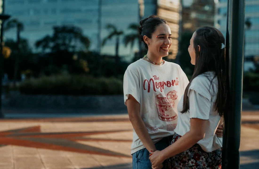 Two women wearing white custom graphic T-shirts outdoors for a screen printing vs DTF comparison